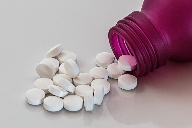 Biele tabletky vysypané z cyklámenovej plastovej fľaštičky.jpg